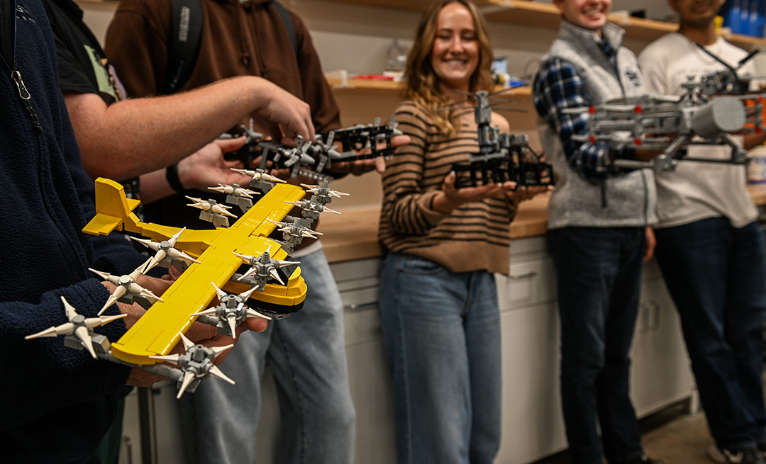 A group of students hold LEGO models of planes in a lab setting