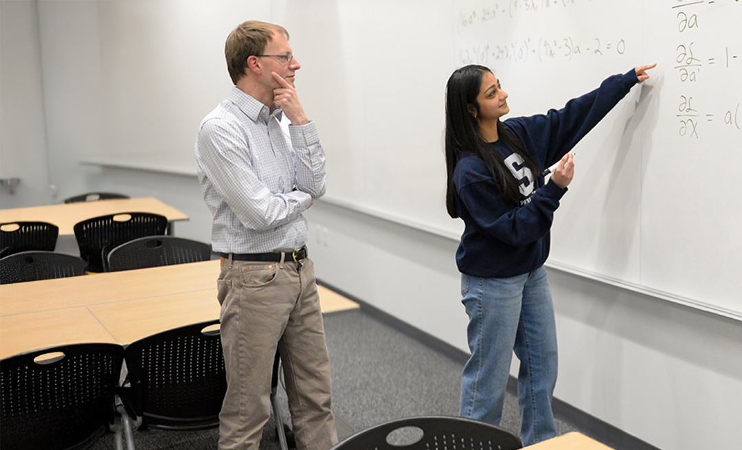 Two individuals examine a math problem on a whiteboard